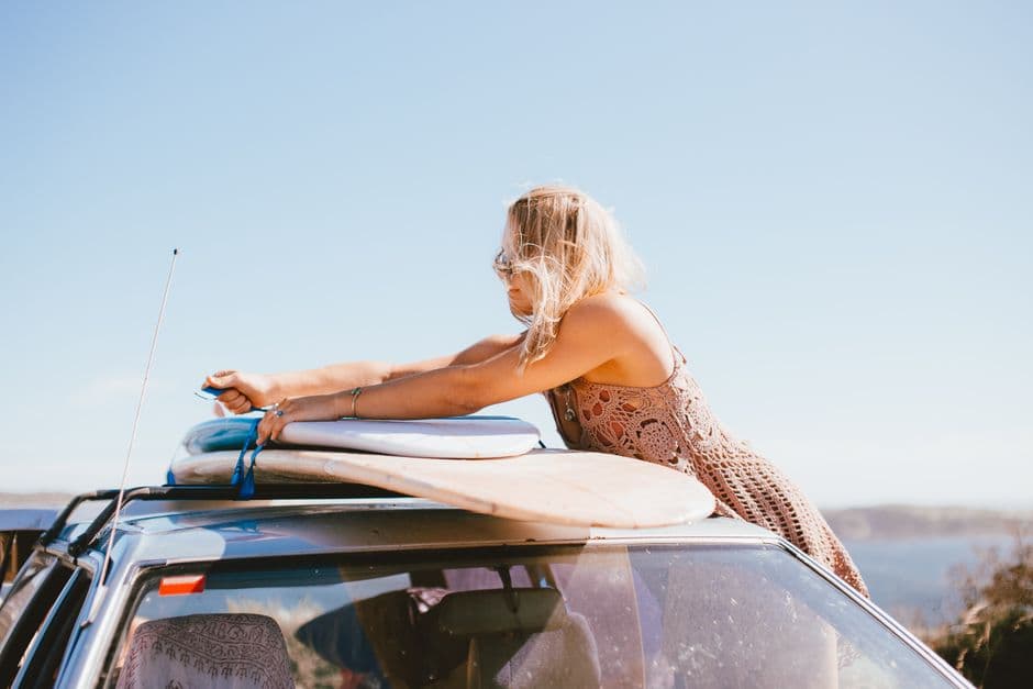 A person strapping surfboards onto a car roof at the beach