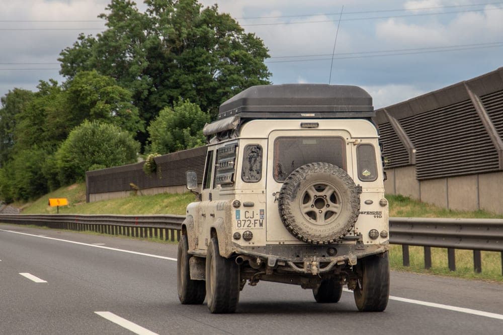 An SUV with aerodynamic crossbars fitted, parked on a gravel road