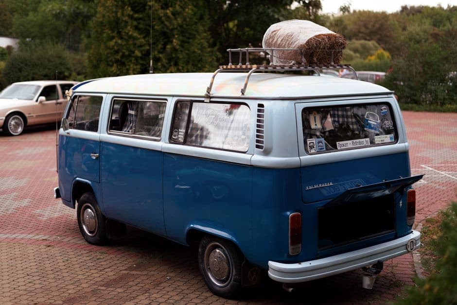 A blue camper van parked outdoors with luggage strapped to its roof rack
