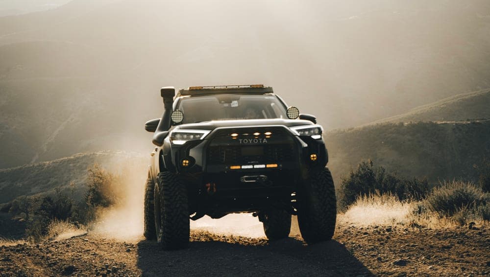 A rugged mid-size SUV parked on a dirt track with gear on the roof